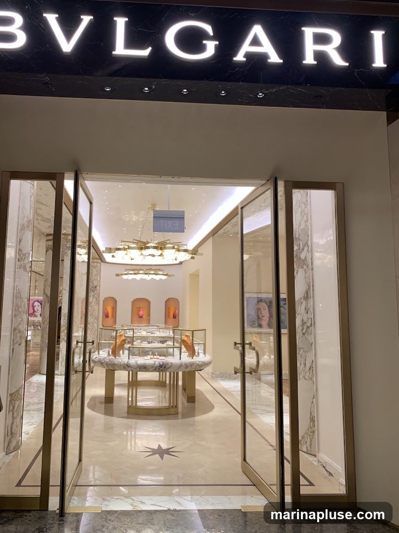 The exterior of a Bulgari store with the brand name illuminated above the entrance. The doors are open, revealing a luxurious interior with display cases and chandeliers.