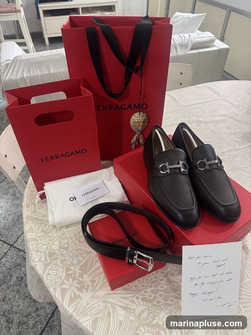 A pair of dark brown Ferragamo loafers, a black Ferragamo belt, two red Ferragamo shopping bags, and a handwritten note are arranged on a patterned tablecloth. The shoes are in their red box, and the belt is on its red box. A white dust bag with a Ferragamo card is also visible. The note reads: "Thank you Monte for your belt and for your appeal. Enjoy you new bell and shoes. May they accompany you well. Happy Holidays! Till next time. SHAI."
