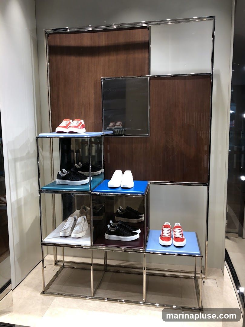 A display of various sneakers on tiered shelves. The shoes include red and white sneakers, black sneakers, and white sneakers. The display has a modern design with metallic frames and colored shelves.