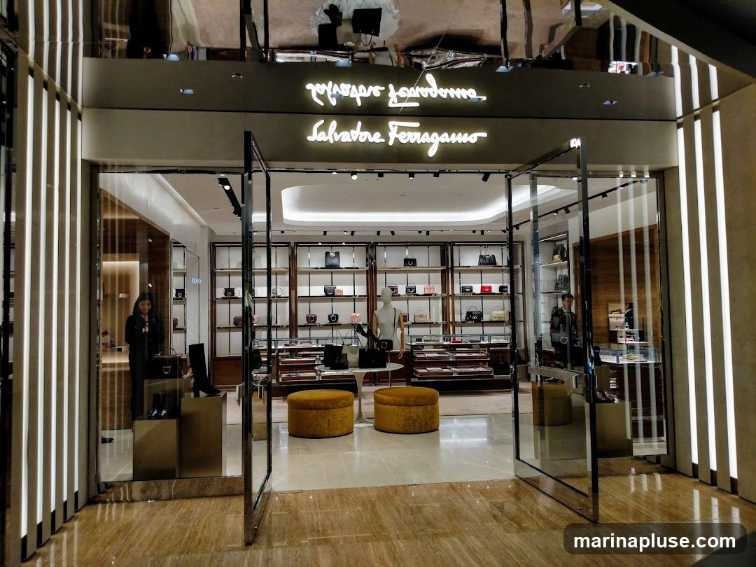 The exterior of a Salvatore Ferragamo store. The entrance features large glass doors and windows, with the store's name illuminated above. Inside, shelves display handbags and other accessories.