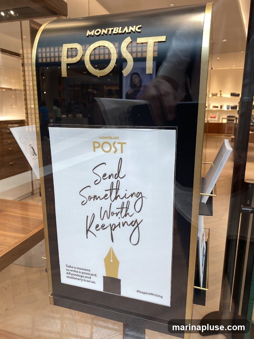 A display stand for Montblanc Post, featuring the slogan "Send Something Worth Keeping." It encourages customers to write a postcard, with postage and stationery provided. The display includes the Montblanc logo and the hashtag #InspireWriting. The background shows the interior of a Montblanc store.