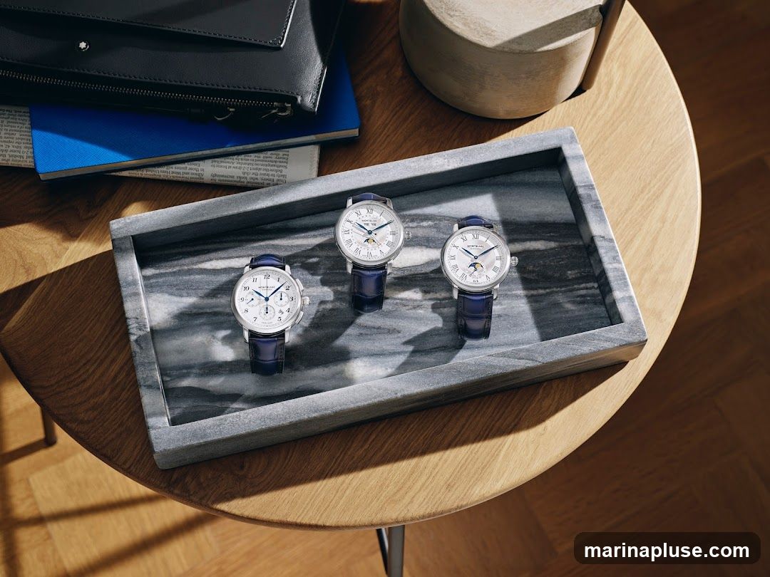 Three Montblanc watches with blue leather straps are displayed on a marble tray on a wooden table. A black leather portfolio and a blue notebook are placed behind the tray.