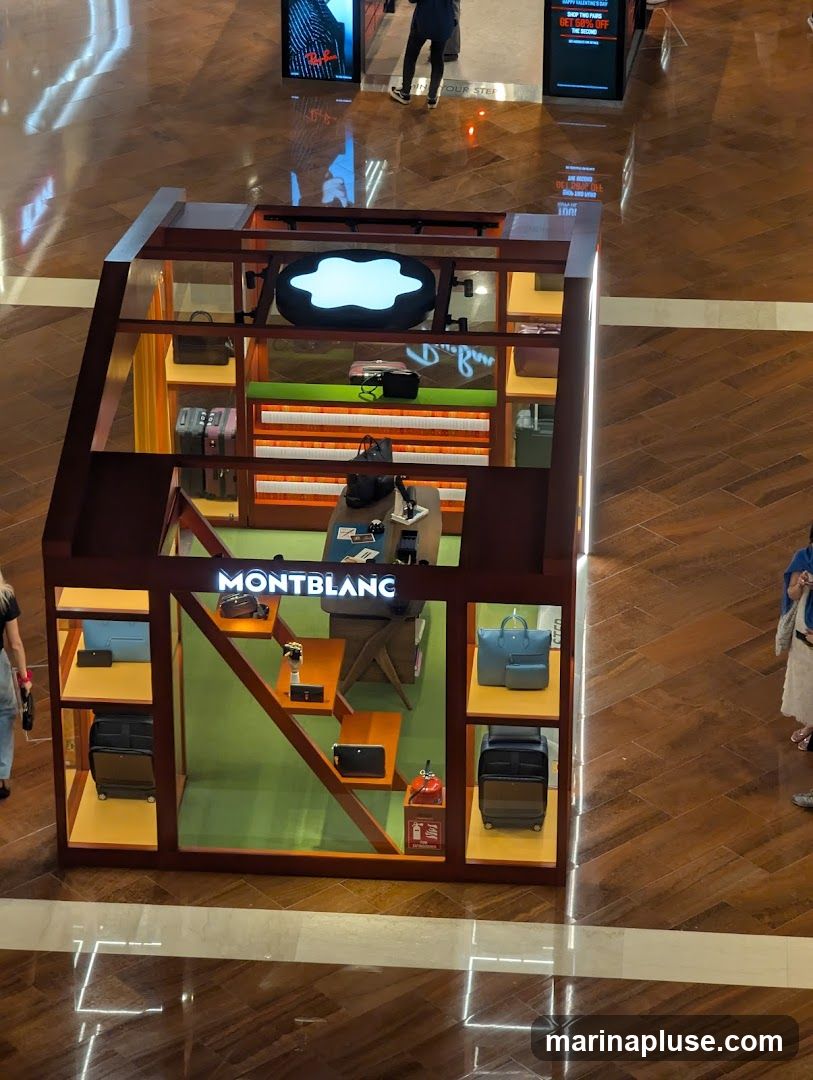 A retail display booth for Montblanc products, featuring various bags, luggage, and accessories. The booth has a modern design with wooden accents and illuminated shelving. The Montblanc logo is prominently displayed above the entrance.