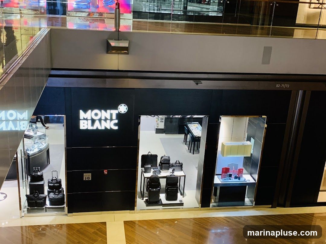 A view from above of a Montblanc store entrance in a mall. The store has a black facade with the Montblanc logo prominently displayed in white. Inside, various bags and display cases with merchandise are visible.