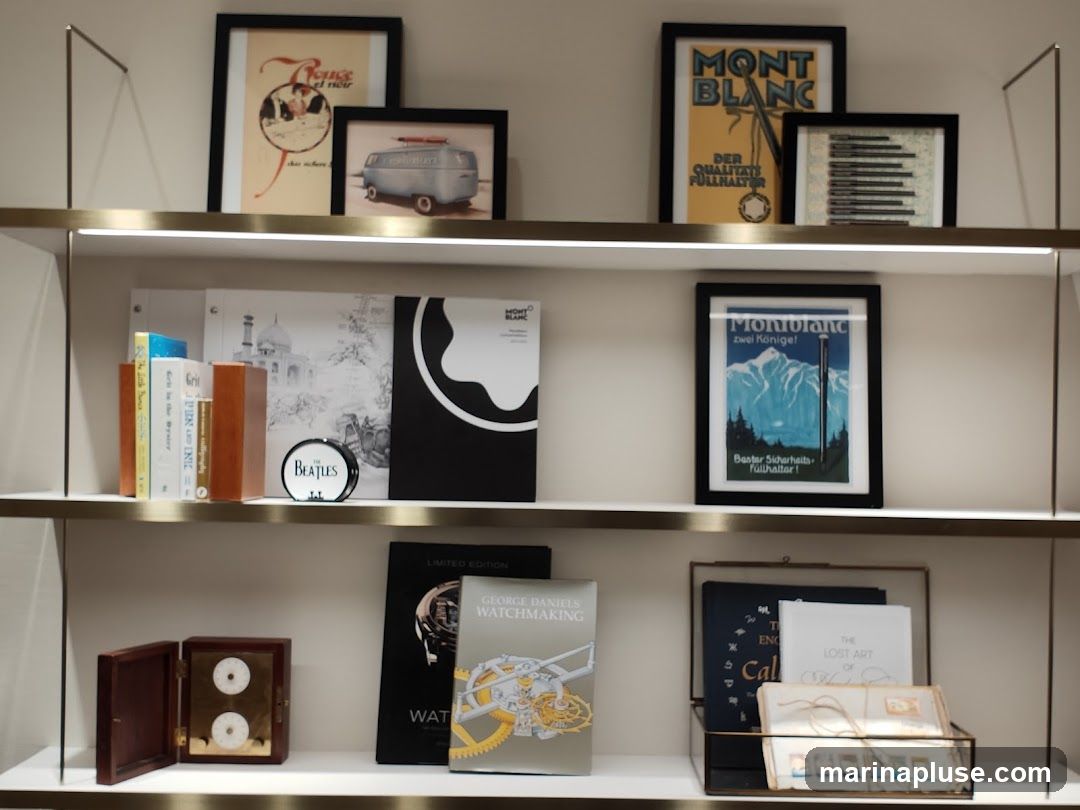 A shelf displaying various items, including framed posters, books, and decorative objects. One poster features the Montblanc logo and text in German, another shows a mountain landscape with a Montblanc pen. There are also books with titles like