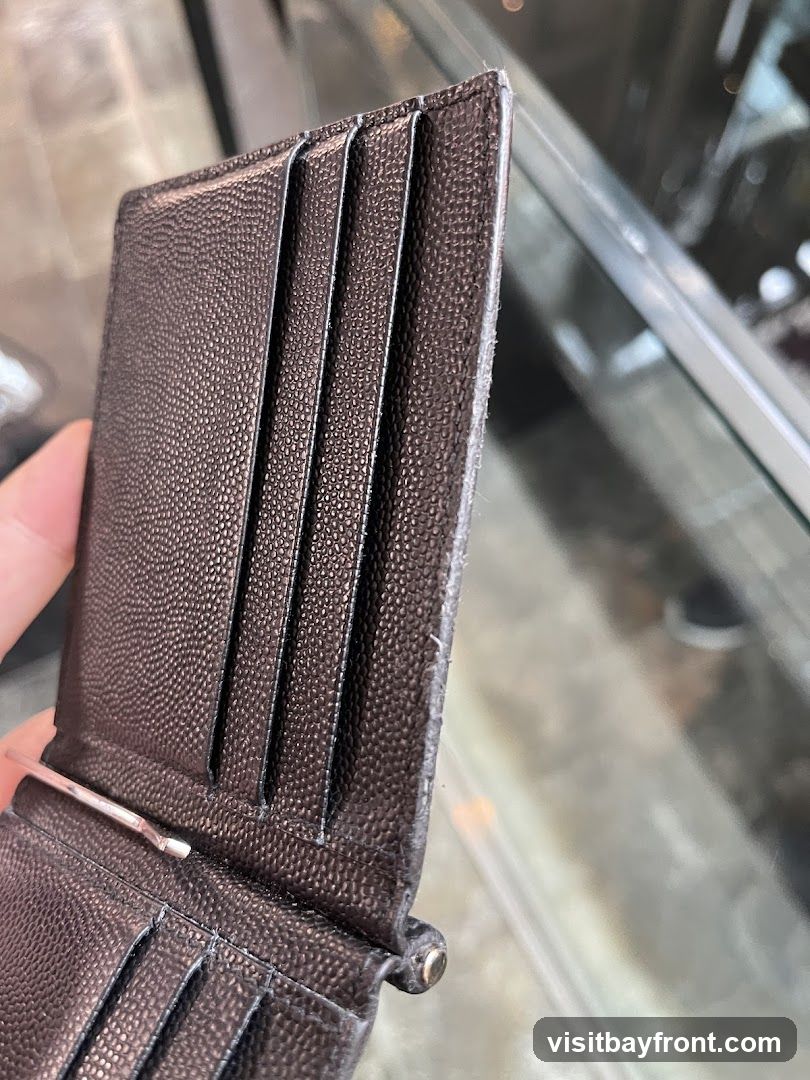 A close-up shot of a person holding a brown textured wallet with multiple card slots and a money clip. The background appears to be a blurred interior with glass displays.