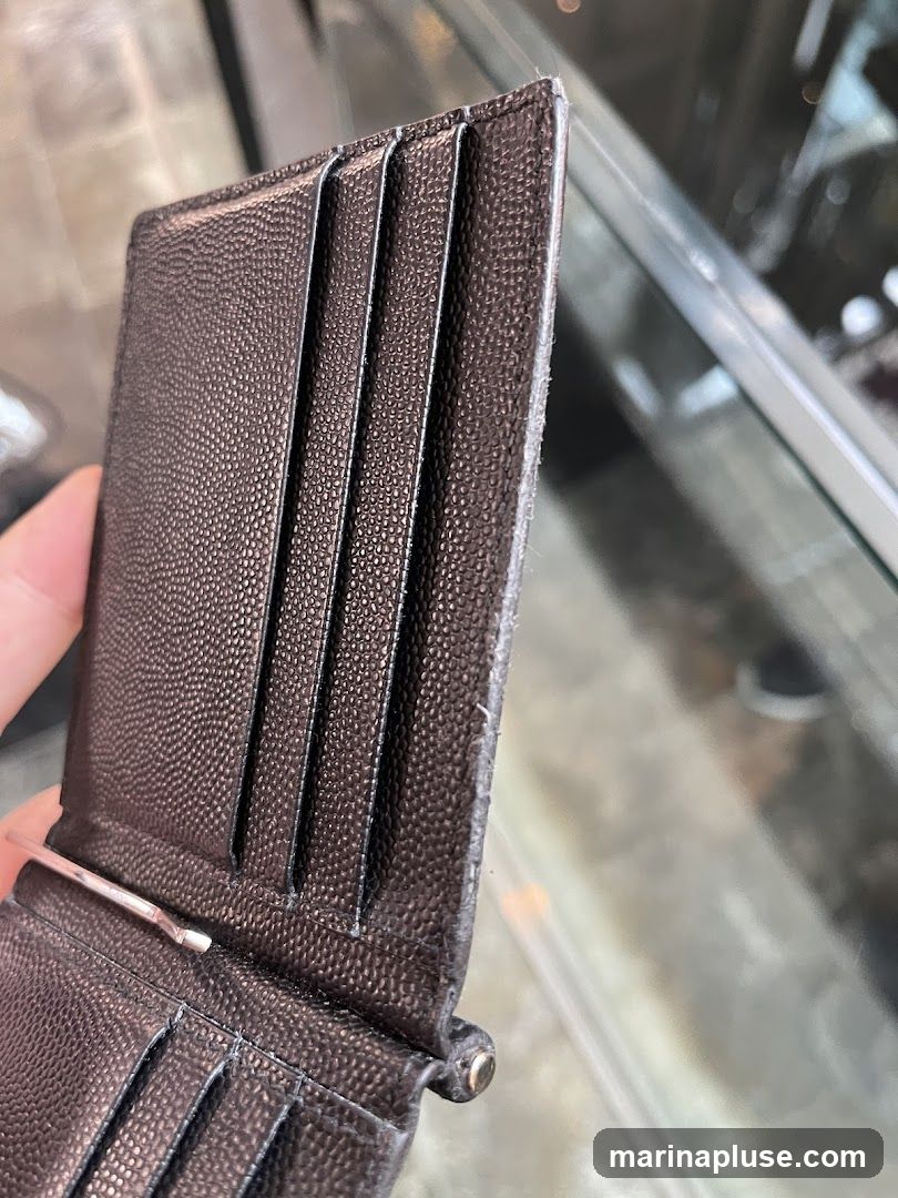 A close-up shot of a person holding a brown textured wallet with multiple card slots and a money clip. The background appears to be a blurred interior with glass displays.