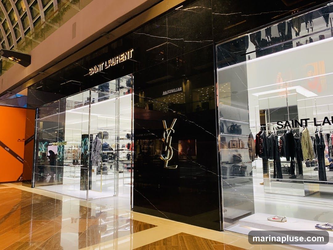 The exterior of a Saint Laurent store with a black marble facade and large glass windows displaying clothing and accessories. The Saint Laurent logo is prominently displayed in gold.