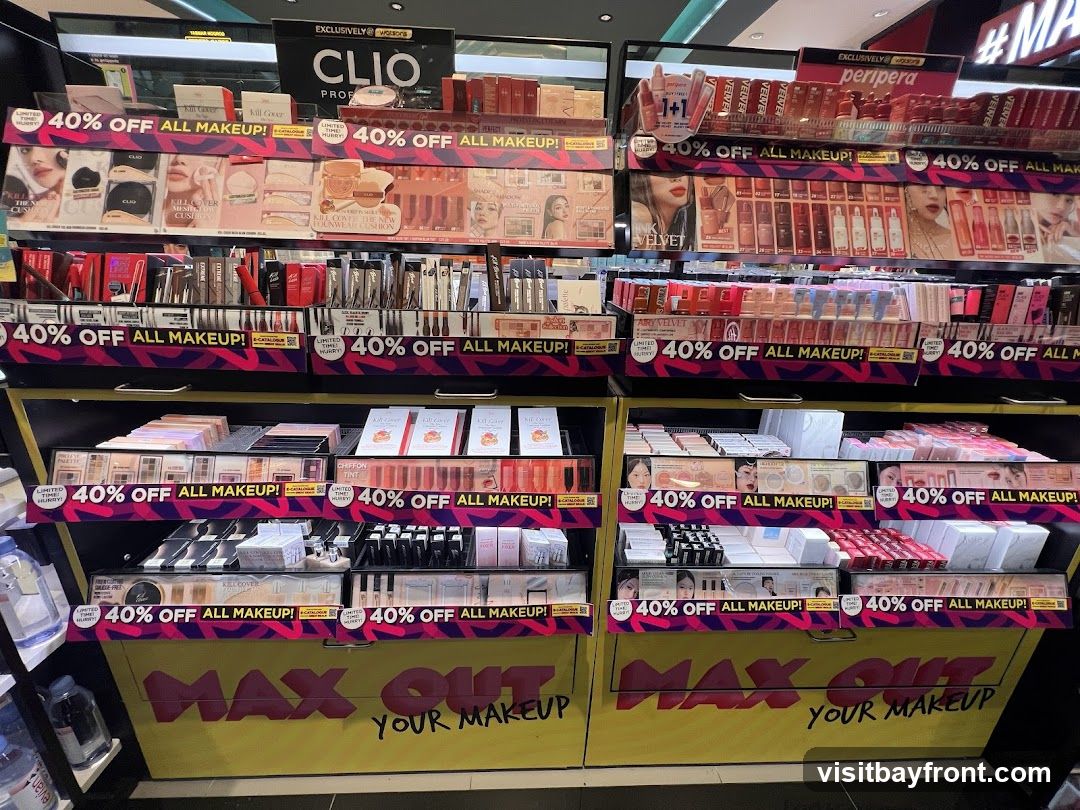 A retail display featuring various makeup products, primarily from brands like CLIO and Peripera. The display is organized on shelves with prominent signage indicating "40% OFF ALL MAKEUP!" and "MAX OUT YOUR MAKEUP!". Products include foundations, lipsticks, eyeshadow palettes, and other cosmetics.
