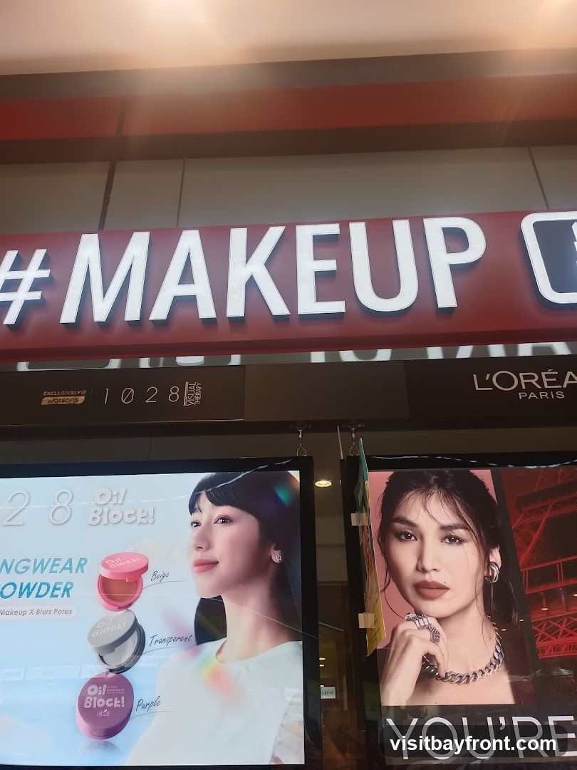 A store display featuring makeup products and advertisements. The main sign reads "#MAKEUP C". Below, there are two large advertisements. The left one showcases "Oil Block! Longwear Powder" with images of the product in beige, transparent, and purple shades, alongside a model. The right advertisement features another model and the text "YOU'RE". The L'Oréal Paris logo is also visible.