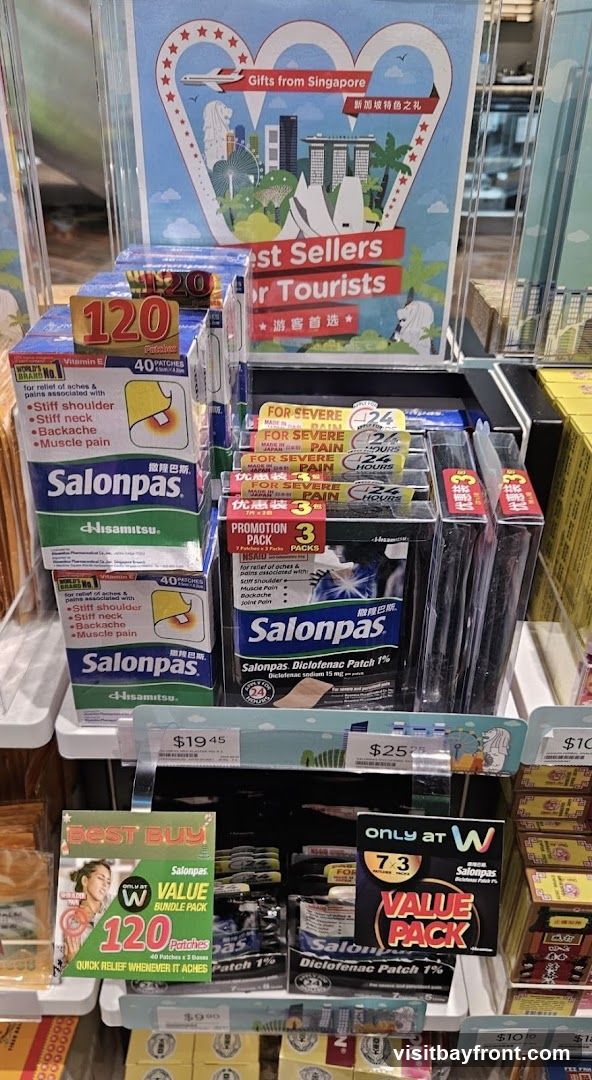 A display of Salonpas pain relief patches, including various pack sizes and promotions. A sign at the top advertises "Best Sellers for Tourists" with images of Singapore landmarks.