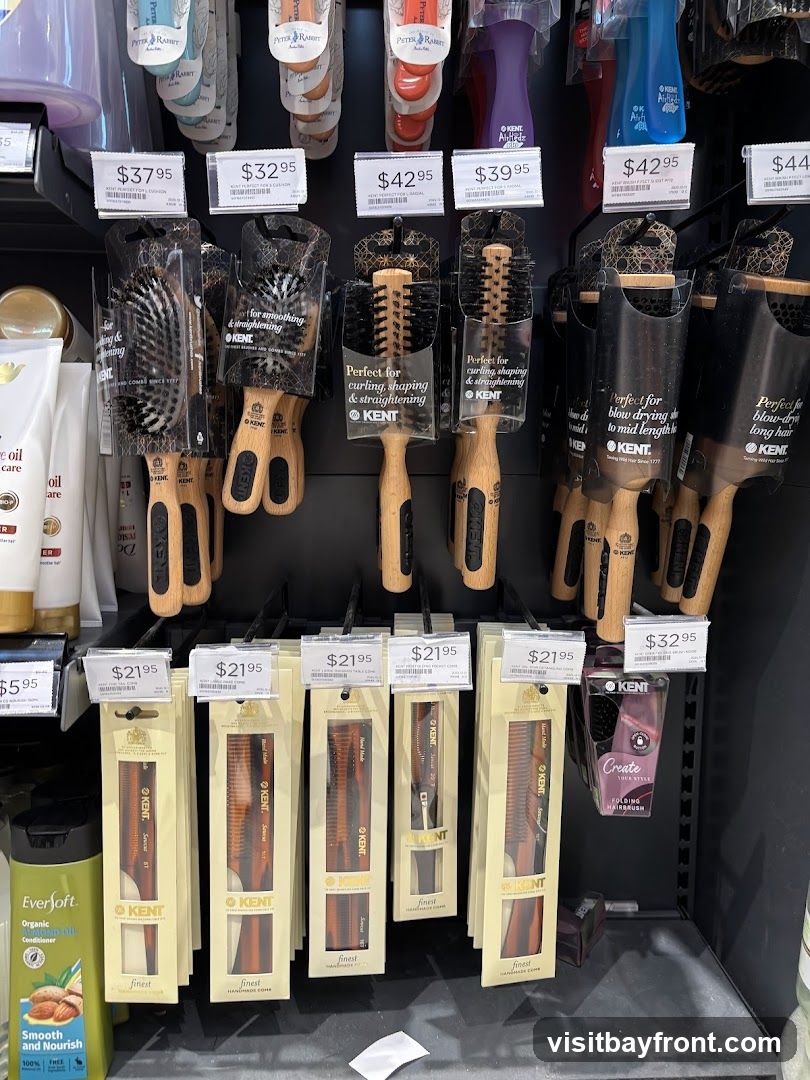 A display of various hair brushes and combs from the brand KENT. The brushes are of different types, including cushion brushes and radial brushes, with wooden handles and bristles. The combs are also made of tortoiseshell-patterned material. Prices are displayed for each item.