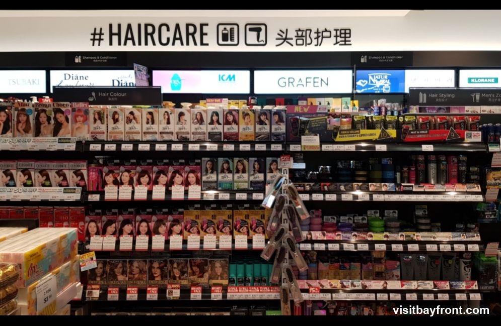 A retail display featuring a wide variety of hair care products, including hair color, shampoos, conditioners, and styling products. Brands like Tsubaki, Diane, ICM, Grafen, Natur, and Klorane are visible. The display is organized on shelves with clear signage indicating product categories.