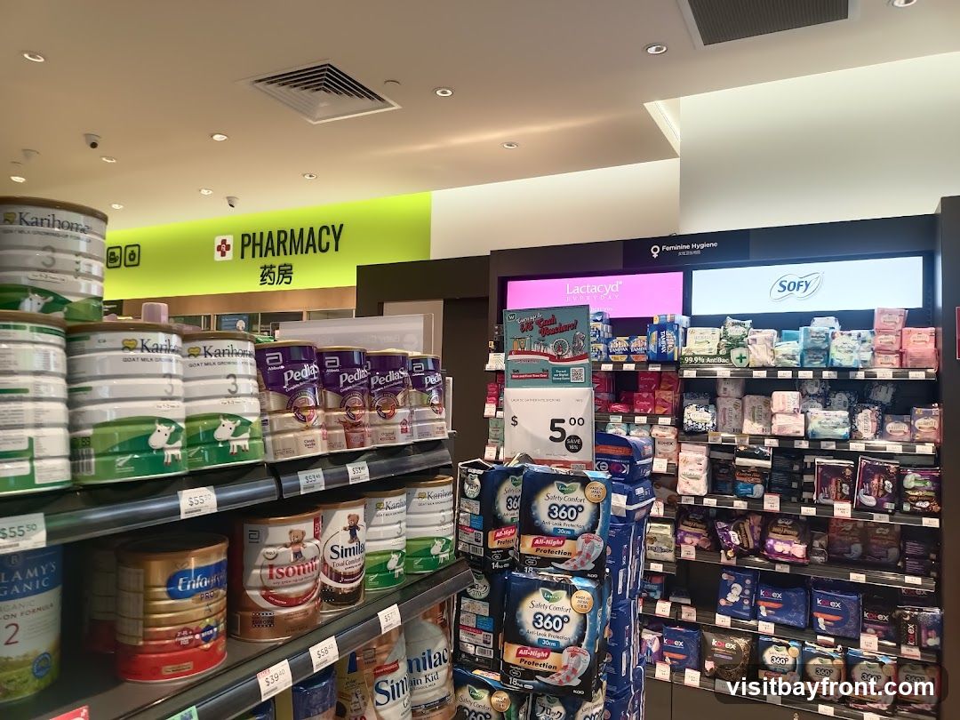 Shelves stocked with baby formula, feminine hygiene products, and other health and personal care items. A prominent sign reads "PHARMACY" in English and Chinese.