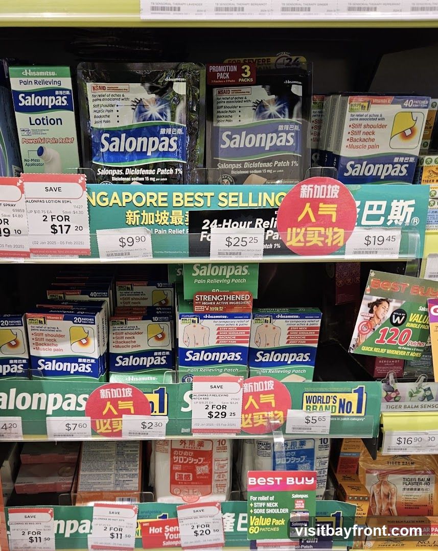 A shelf display of various Salonpas pain relief products, including lotions and patches. Promotional signage highlights "Singapore Best Selling" and "World's No. 1 Brand". Several products are on sale with prices indicated.