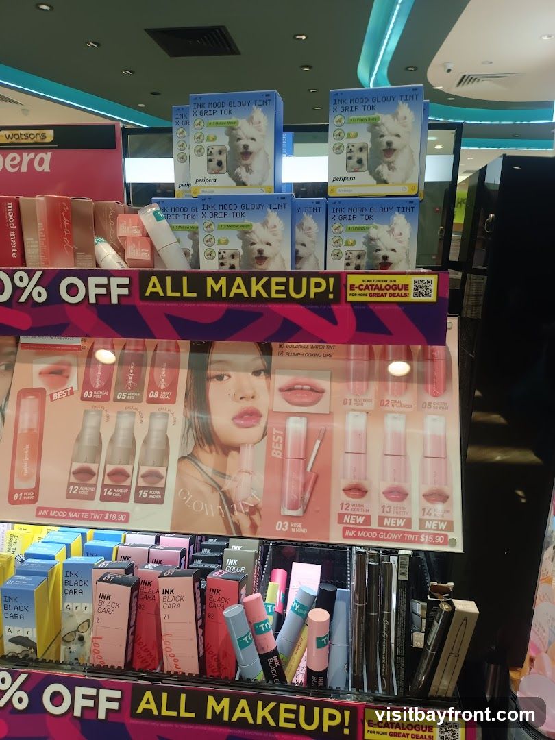 A display of various makeup products, including lip tints and mascaras, with a prominent "50% OFF ALL MAKEUP!" banner. Several products feature images of dogs on their packaging. An e-catalogue QR code is also visible.