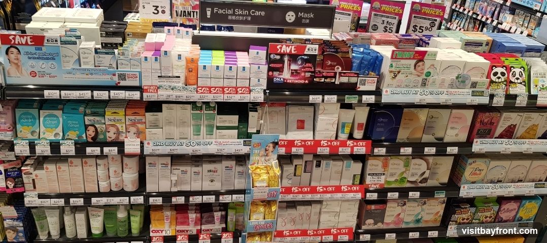 A retail display featuring a wide variety of skincare products, including facial masks, serums, creams, and cleansers. Various promotional signs indicate discounts such as 'SAVE', '2ND BUY AT 50% OFF', and '15% OFF'. Brands visible include Nexcare, Derma Angel, and others. The display is organized on multiple shelves with clear pricing and product information.