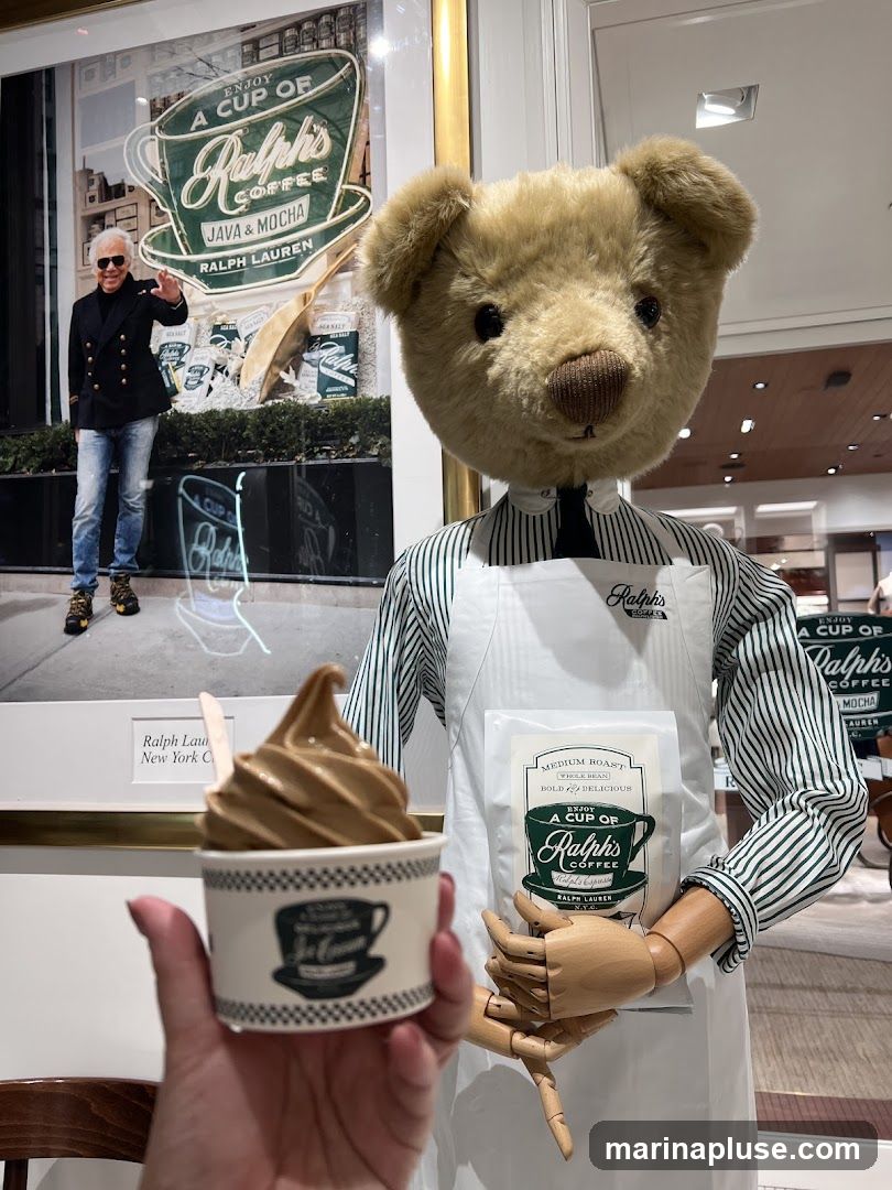 A teddy bear dressed in a striped shirt and apron stands in front of a display featuring Ralph Lauren's coffee. The display includes a large graphic of a coffee cup with the text "Enjoy a Cup of Ralph's Coffee Java & Mocha Ralph Lauren," a picture of Ralph Lauren, and bags of coffee beans. A hand holds a cup of soft-serve ice cream with the Ralph's Coffee logo.
