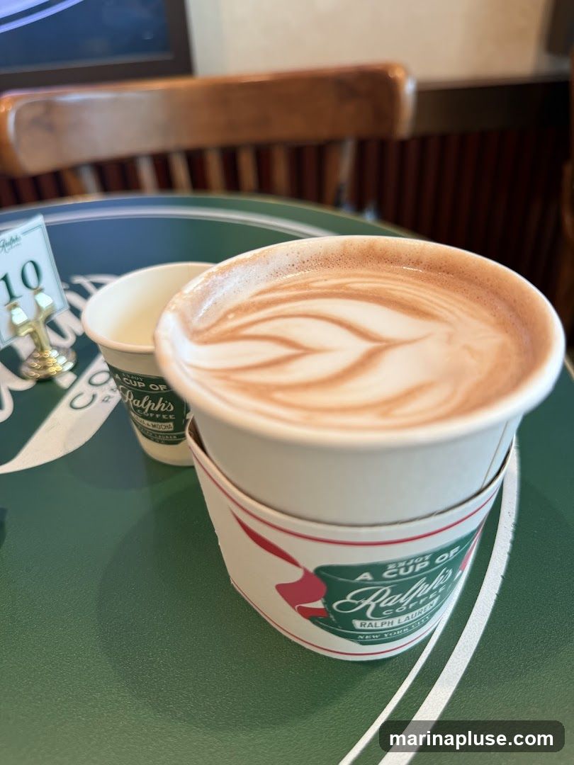 A close-up shot of a coffee cup with latte art, placed on a green table. Another smaller cup is visible behind it. A table number '10' is also present. The coffee cup has a sleeve with the Ralph's Coffee logo.