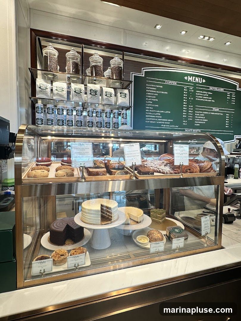 A display case filled with various baked goods, including cakes, cookies, pastries, and bread. Shelves above hold bags of coffee and jars of coffee beans. A menu board is visible on the right side.