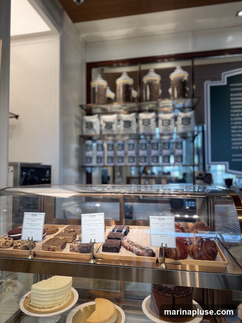 A display case filled with various baked goods, including cakes, brownies, cookies, and croissants. Behind the display, shelves are stocked with bags of coffee beans and jars of coffee.