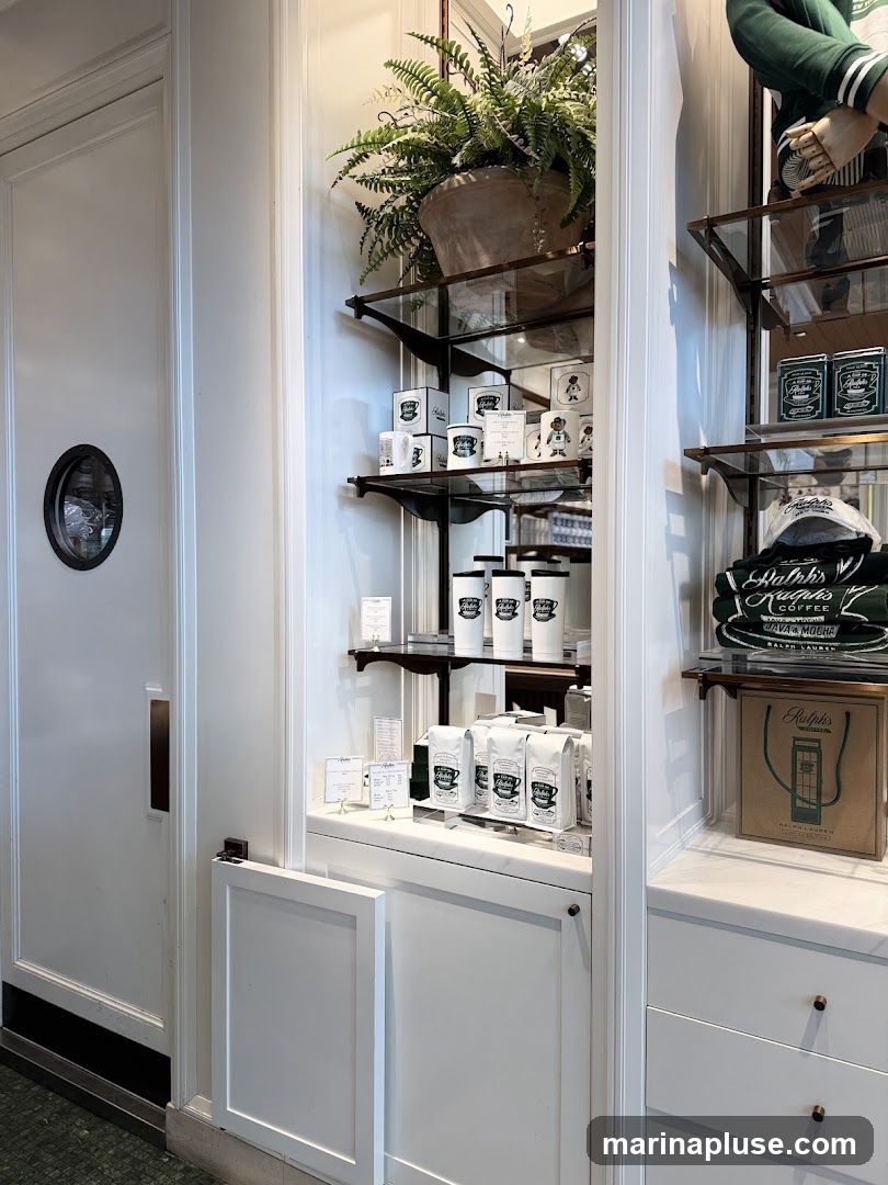 A display shelf filled with Ralph Lauren branded coffee merchandise, including bags of coffee beans, mugs, and hats. A large potted fern sits on the top shelf. The display is set against a white paneled wall with a door on the left.