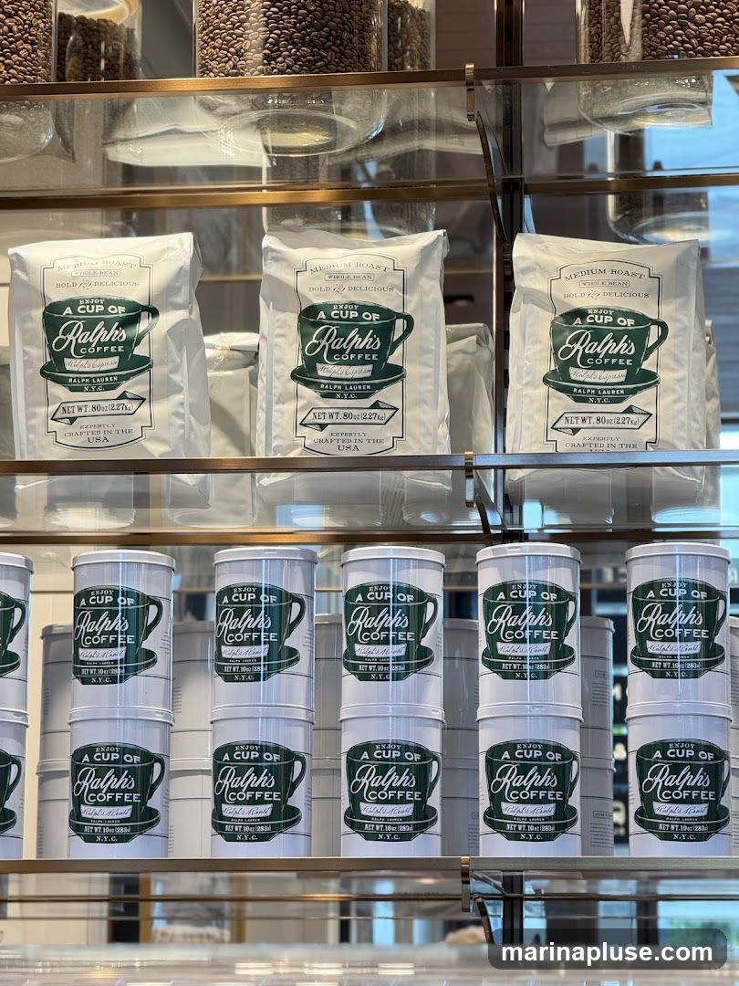 Display of bags and tins of Ralph's Coffee, a brand by Ralph Lauren. The bags are labeled 'Medium Roast Whole Bean Bold & Delicious' and contain 8 oz (2.27kg) of coffee, expertly crafted in the USA. The tins are smaller and also feature the Ralph's Coffee branding. Jars of coffee beans are visible on the top shelf.