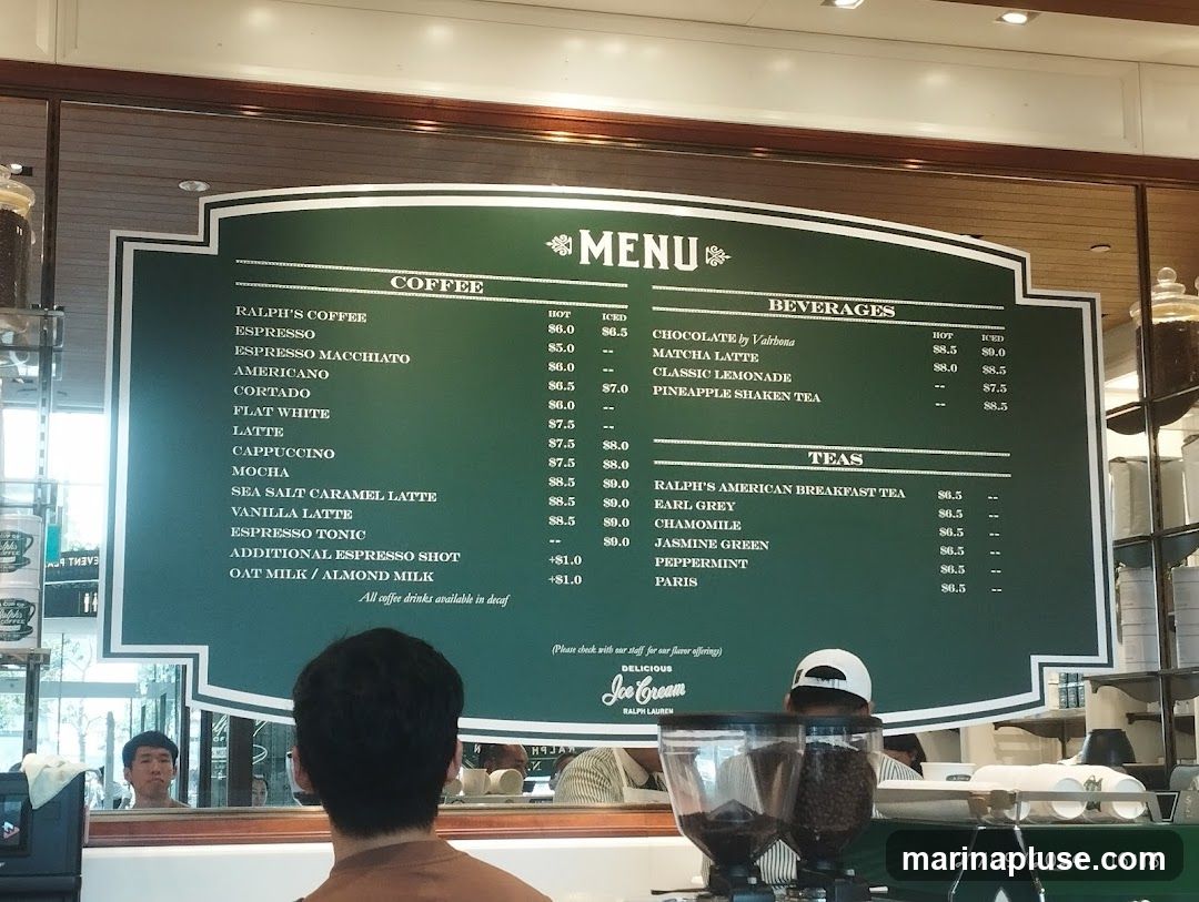 A green menu board with white lettering displays coffee, beverages, and tea options. The menu is divided into sections: Coffee, Beverages, and Teas. Coffee options include Ralph's Coffee, Espresso, Americano, Cortado, Flat White, Latte, Cappuccino, Mocha, Sea Salt Caramel Latte, Vanilla Latte, Espresso Tonic, and Additional Espresso Shot. Beverage options include Chocolate by Valrhona, Matcha Latte, Classic Lemonade, and Pineapple Shaken Tea. Tea options include Ralph's American Breakfast Tea, Earl Grey, Chamomile, Jasmine Green, Peppermint, and Paris. Prices are listed for hot and iced versions of some drinks.