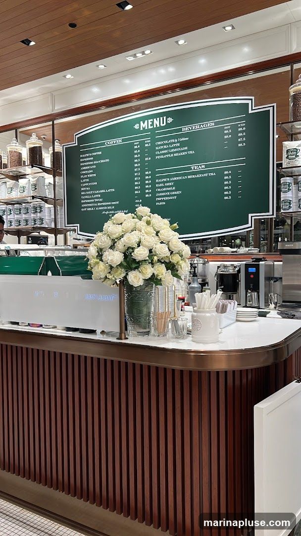 A green menu board with white text lists coffee, beverages, and teas. A large vase of white roses sits on the counter in front of the menu.