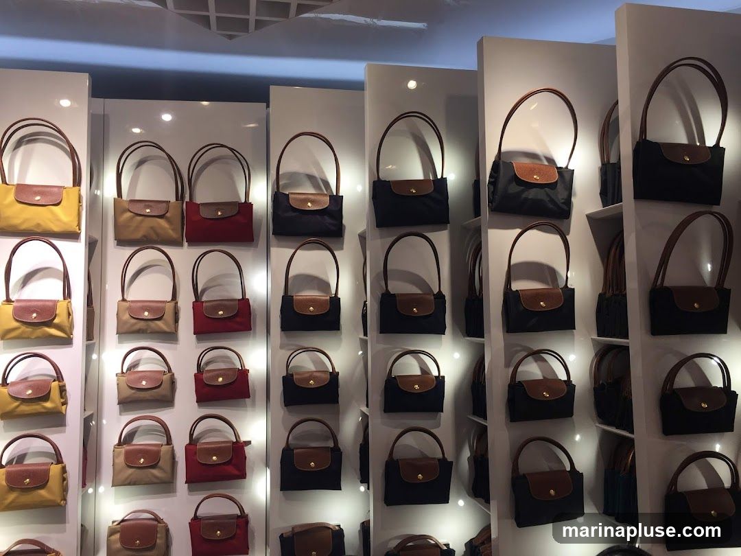 A wall display of various handbags in different colors and sizes. The handbags are arranged in rows and columns on white shelves. Some of the colors visible include yellow, tan, red, and navy blue. Each handbag features a brown leather flap closure with a snap button.