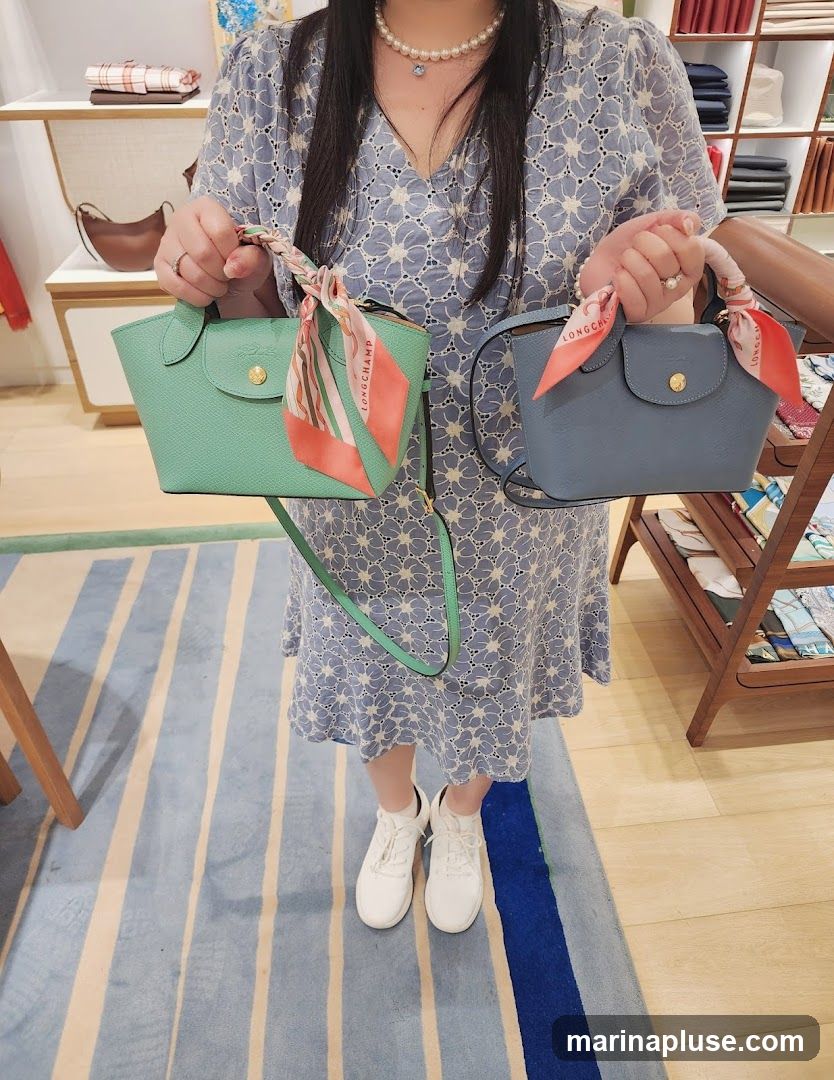 A woman in a blue floral dress and white sneakers holds two small handbags, one mint green and one light blue. Both bags have scarves tied to their handles. The background shows a retail store interior with shelves displaying merchandise.
