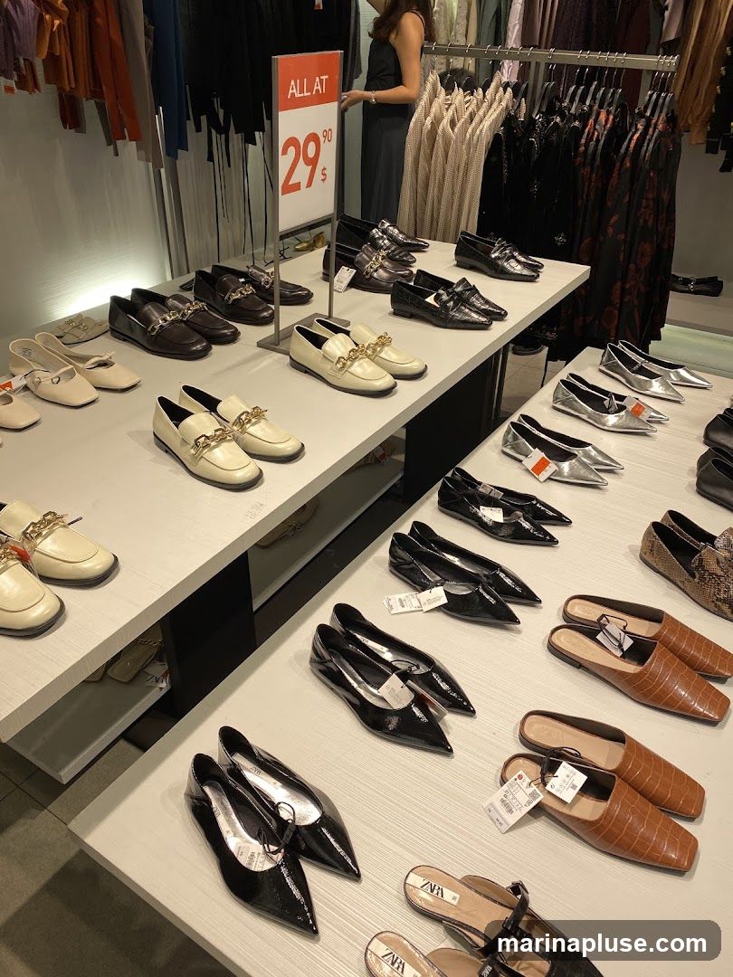 A display of various women's shoes, including loafers, flats, and mules, arranged on white tables. A sign in the background indicates "ALL AT 29.90". Clothing racks with dresses and tops are visible behind the shoe display.