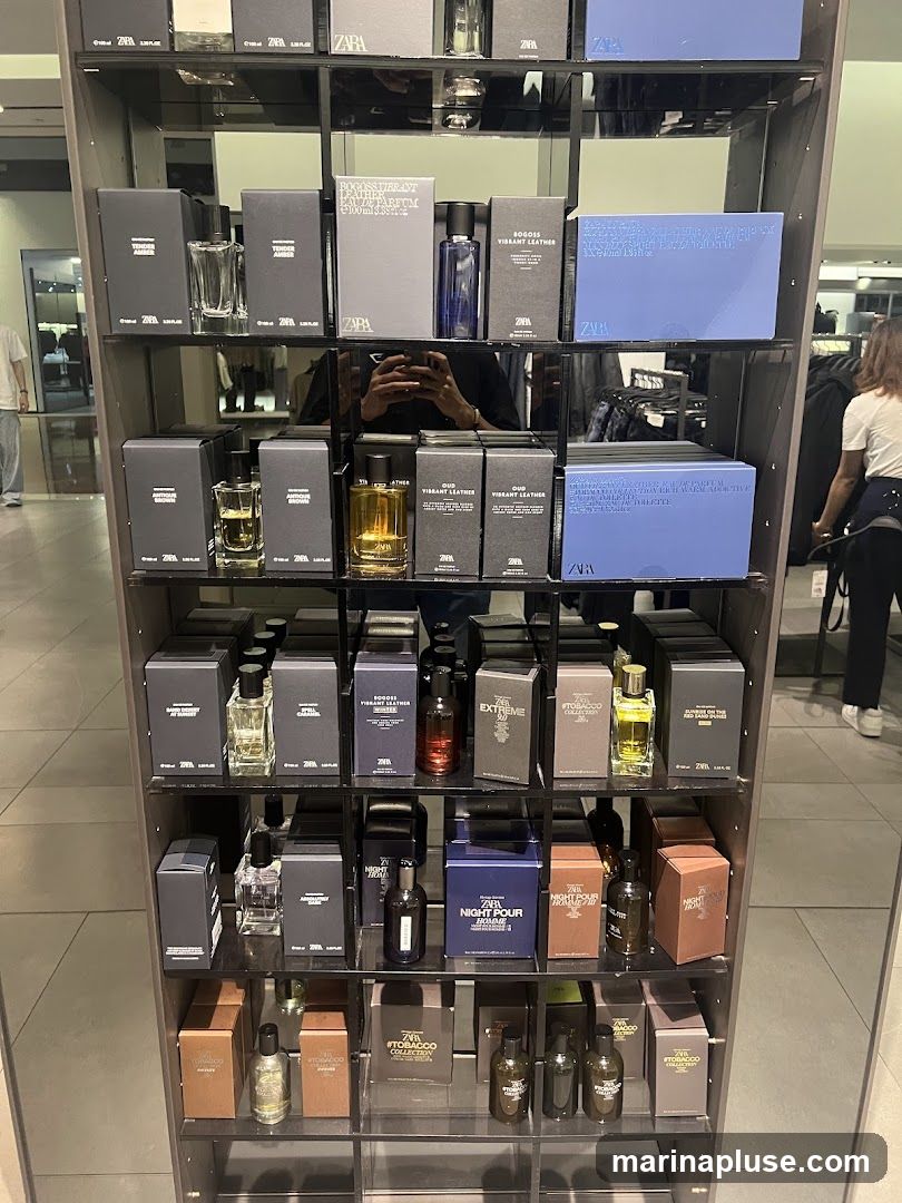 A display shelf filled with various Zara perfumes in boxes and bottles. The perfumes are arranged in a grid on multiple shelves. Some of the visible labels include 'Tender Amber', 'Bogoss Vibrant Leather', '#Tobacco Collection', 'Extreme', and 'Night Pour Homme'. The background shows a retail store environment with clothing racks and other displays.