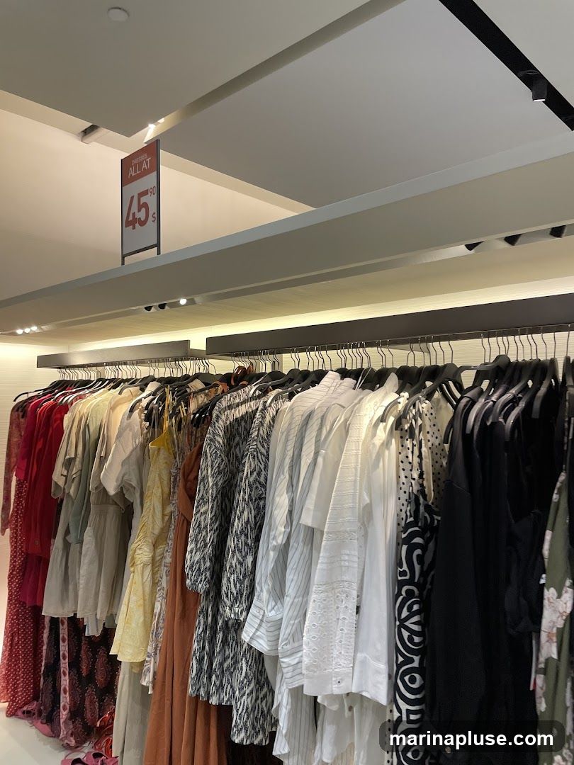 A rack of women's dresses and tops hangs in a store. A sign indicates that dresses are all at 45.90.