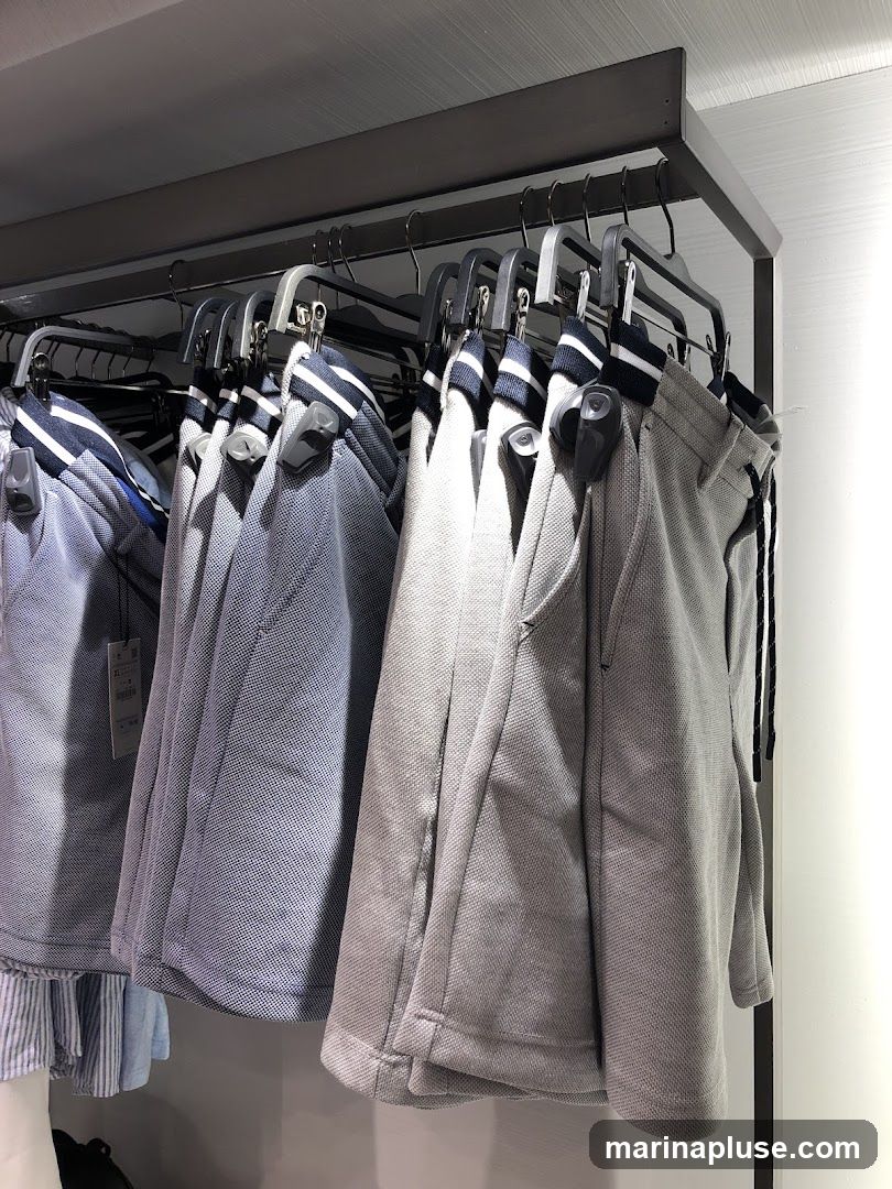 A rack of shorts hangs on hangers in a store. The shorts are in various shades of blue and gray, with some featuring striped cuffs. Security tags are attached to some of the garments.