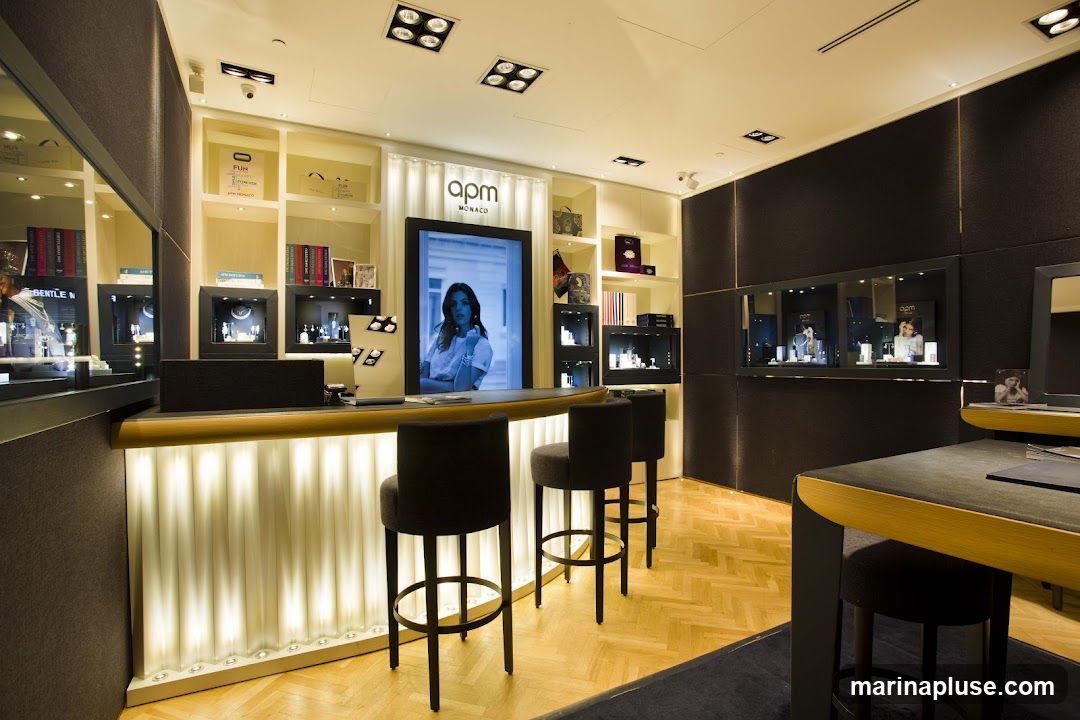 The interior of a modern jewelry store with display cases, a counter, and seating. The store features a large screen displaying a model, and shelves stocked with merchandise. The lighting is bright and highlights the products.