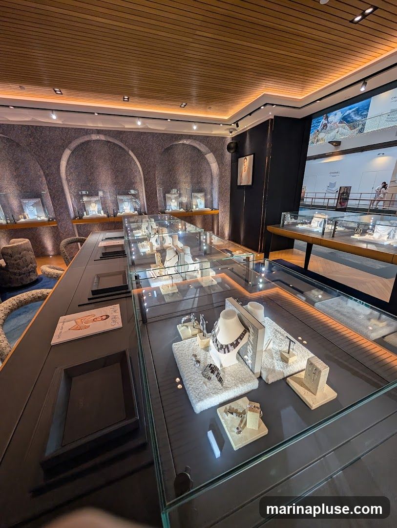 A well-lit jewelry store interior with display cases showcasing necklaces, bracelets, and earrings. The store features arched wall displays, a wooden slatted ceiling, and a large screen displaying advertisements.