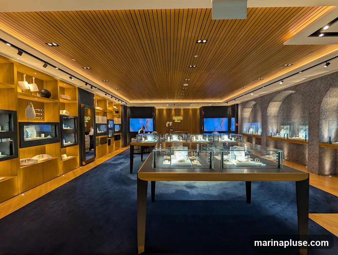 The interior of a modern jewelry store with display cases filled with jewelry. The store features a wooden slatted ceiling, blue carpet, and illuminated shelves displaying accessories. A logo is visible on a screen in the background.