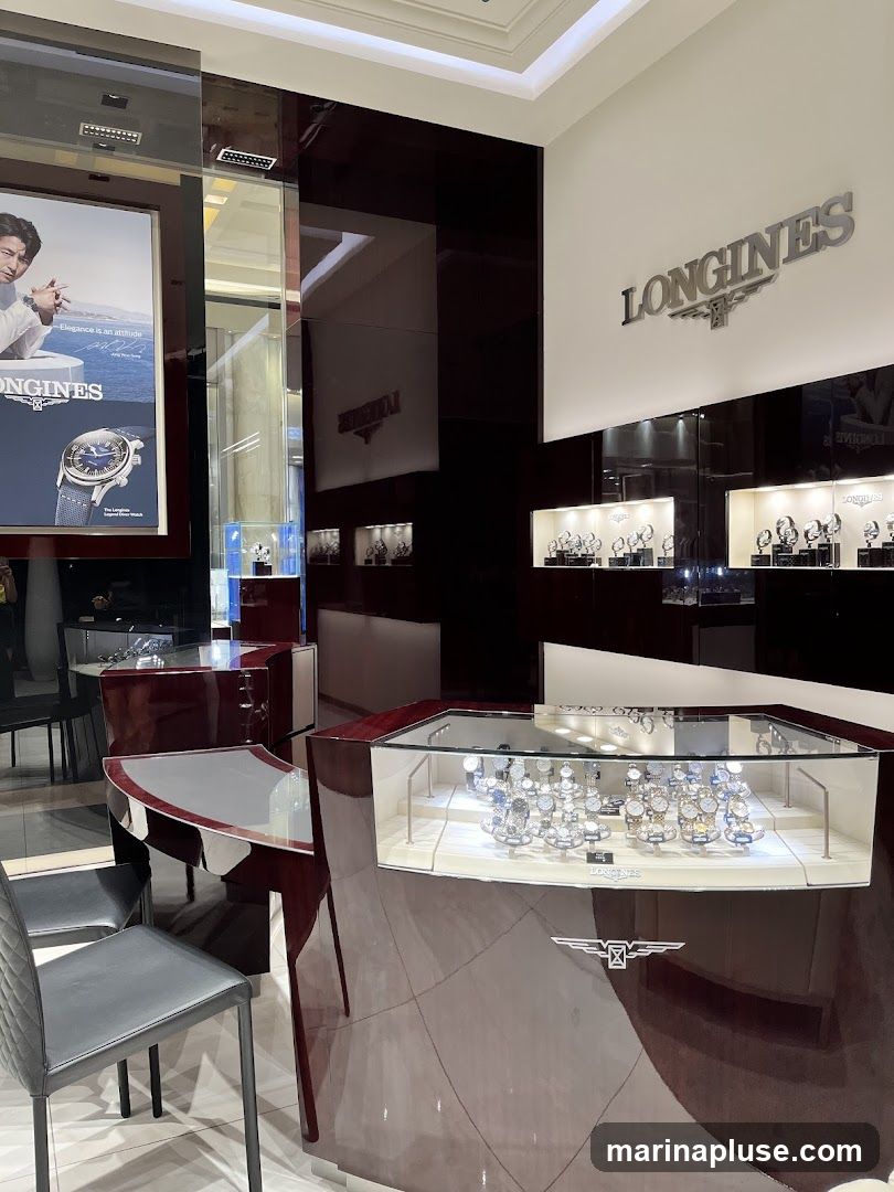 The interior of a Longines watch store, featuring display cases filled with watches, a promotional poster, and branded signage. The store has a modern and luxurious design with dark, glossy surfaces and bright lighting.