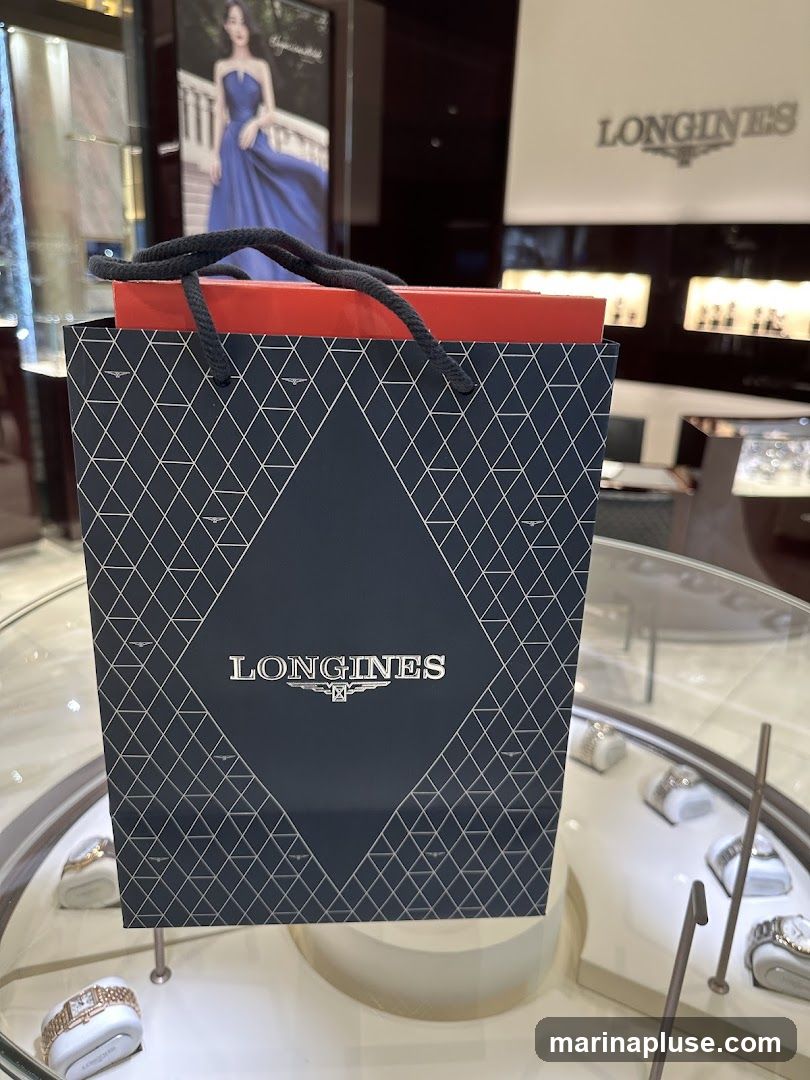 A dark blue Longines shopping bag with a geometric pattern and the brand's logo is placed in front of a display case with watches. In the background, there is a poster of a woman in a blue dress and a Longines sign.