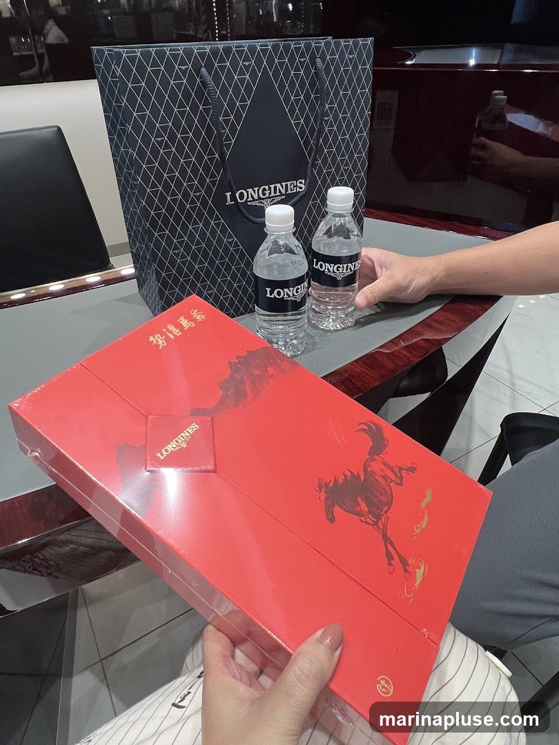 A red box with a Longines logo and horse imagery, a Longines shopping bag, and two bottles of water with Longines labels are on a table.