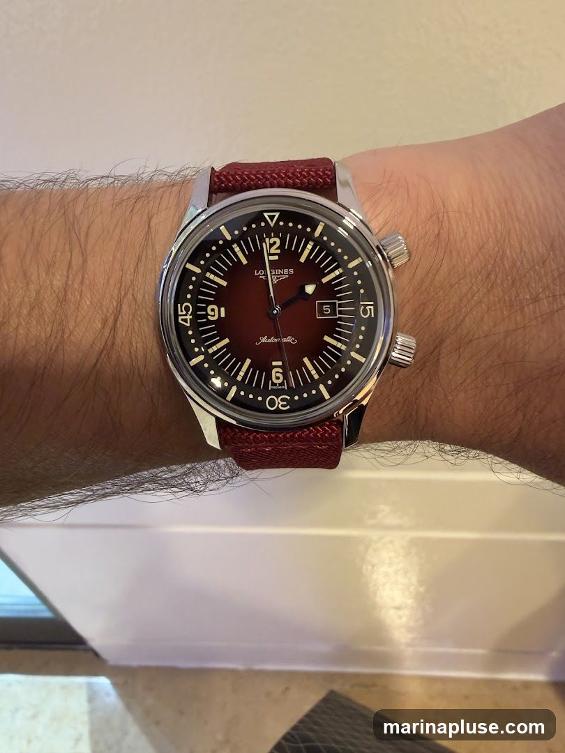 A close-up shot of a Longines automatic watch with a deep red dial and a matching red fabric strap, worn on a person's wrist. The watch features a silver-toned case, a rotating bezel with minute markers, and luminous hands and hour markers. The dial has a date window at the 3 o'clock position. The watch is branded with the Longines logo and the word "Automatic" written in script.