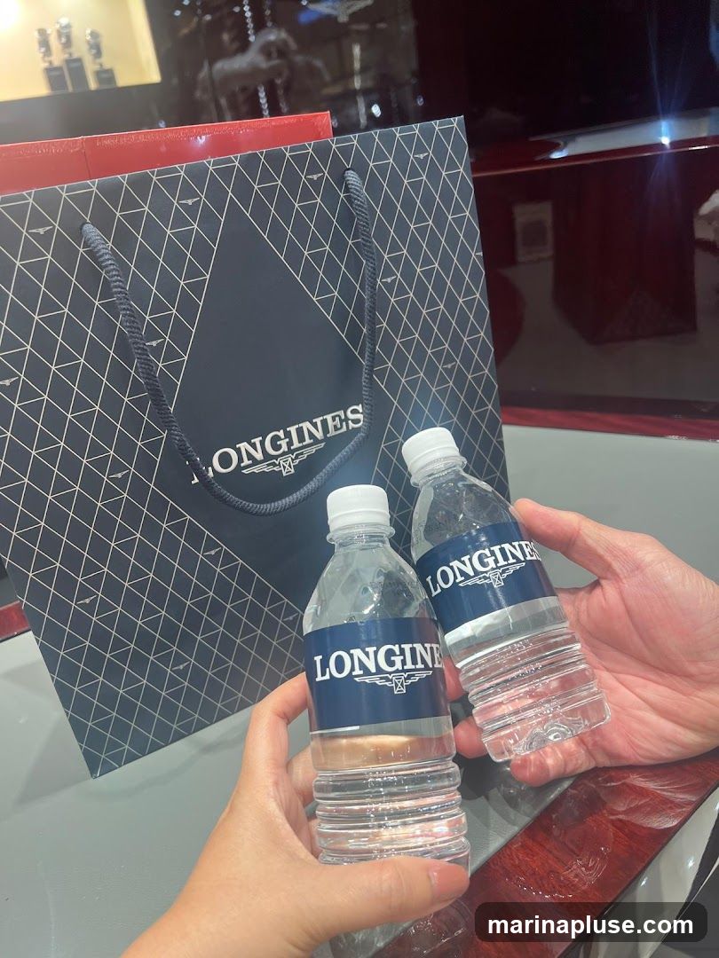 Two bottles of water with Longines branding are held by hands in front of a Longines shopping bag. The background appears to be an interior of a store, possibly a watch shop, with display cases visible.