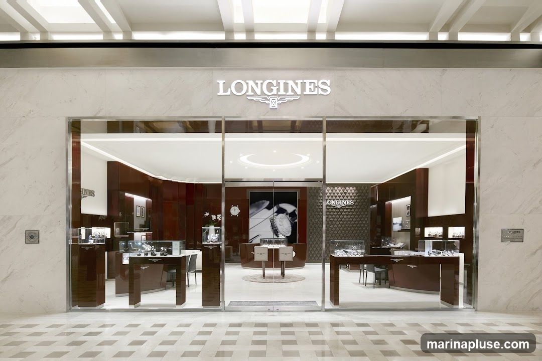 The exterior of a Longines watch store, featuring a large glass facade with the brand's name and logo prominently displayed above the entrance. Inside, display cases showcase watches, and the interior is decorated with dark wood and elegant lighting.