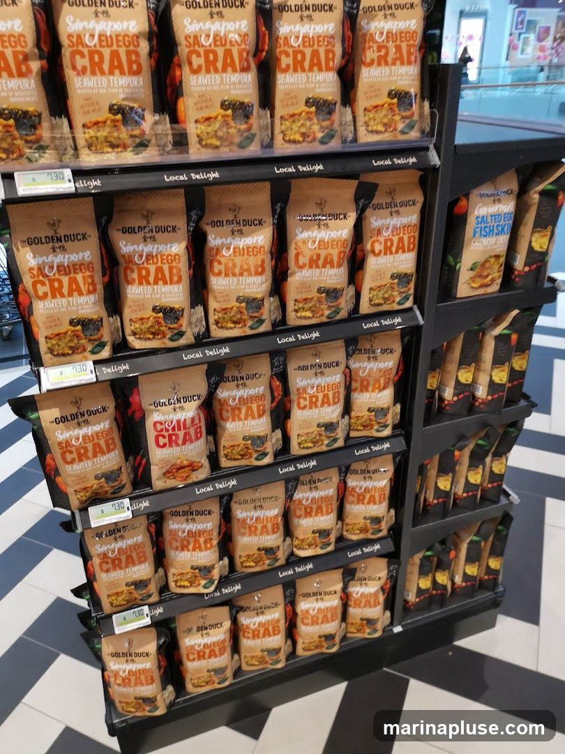 A display shelf filled with various flavors of Golden Duck brand snacks, primarily Singapore Salted Egg Crab Seaweed Tempura. Other visible flavors include Chilli Crab and Salted Egg Fish Skin. The snacks are packaged in brown resealable pouches with prominent branding and images of the product.