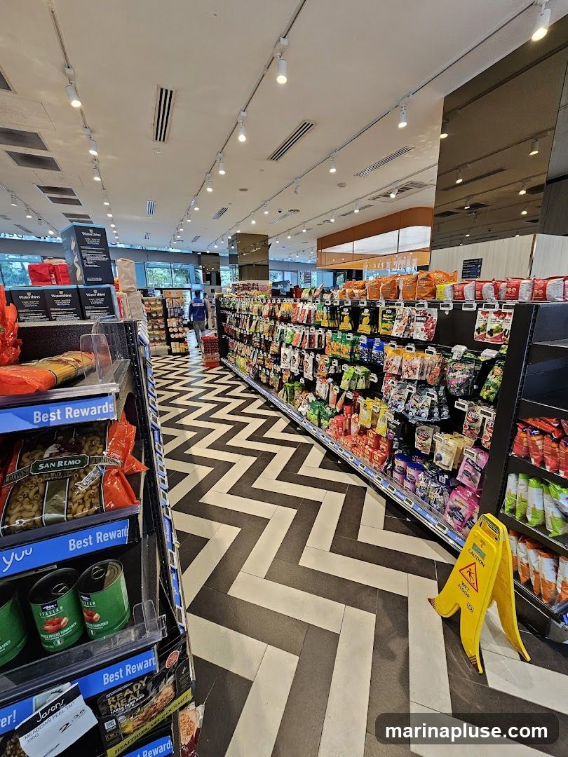 An interior view of a grocery store aisle with shelves stocked with various food items. The floor has a distinctive black and white chevron pattern. A yellow wet floor caution sign is visible on the right side of the aisle.