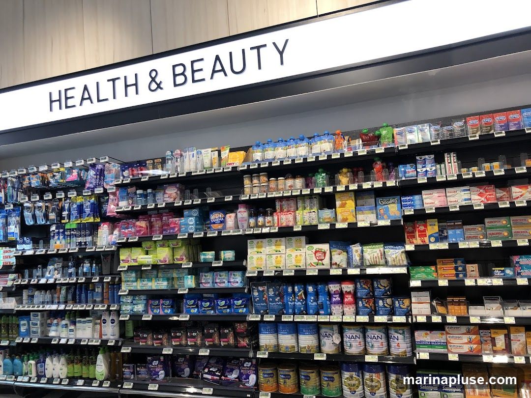 A wide shot of a store aisle labeled "HEALTH & BEAUTY" with shelves stocked with various health and personal care products. The products include baby formula, feminine hygiene products, pain relievers, baby food, toiletries, and other personal care items.