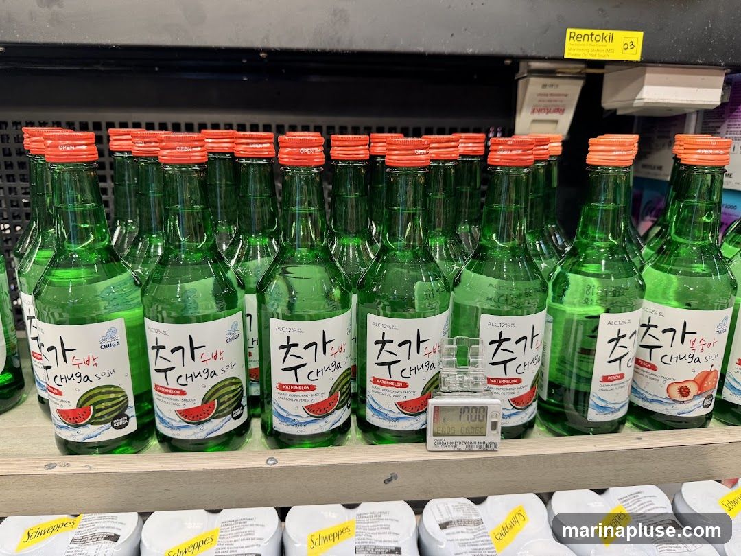 A shelf filled with green bottles of Chuga soju with red caps. The labels indicate watermelon and peach flavors, with an alcohol content of 12%. A digital timer is placed in front of the bottles. Below the soju bottles, there are several packages of Schweppes.