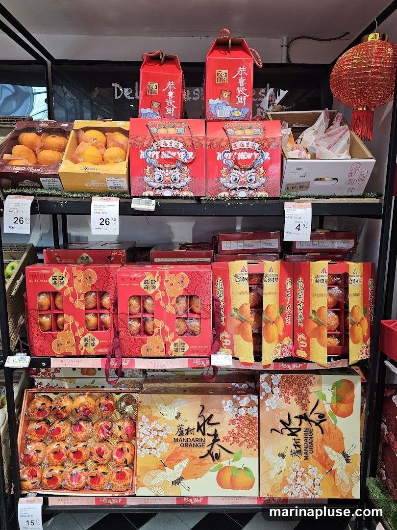 A display of fruits and gift boxes, likely for Chinese New Year. There are boxes of mandarins and oranges, some packaged in decorative red boxes with dragon and crane motifs. Prices are visible for some items.