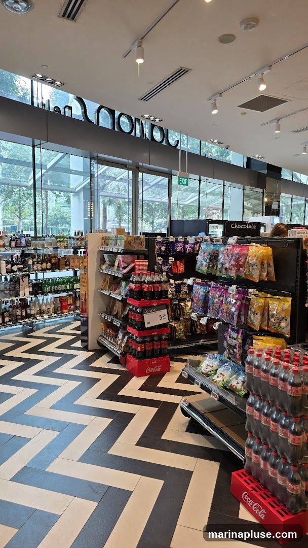 A view inside a brightly lit convenience store with a distinctive black and white chevron patterned floor. Shelves are stocked with various products including bottled drinks, snacks, chocolates, and liquor. A prominent display of Coca-Cola bottles is visible. An 'EXIT' sign is illuminated in green above a glass door.